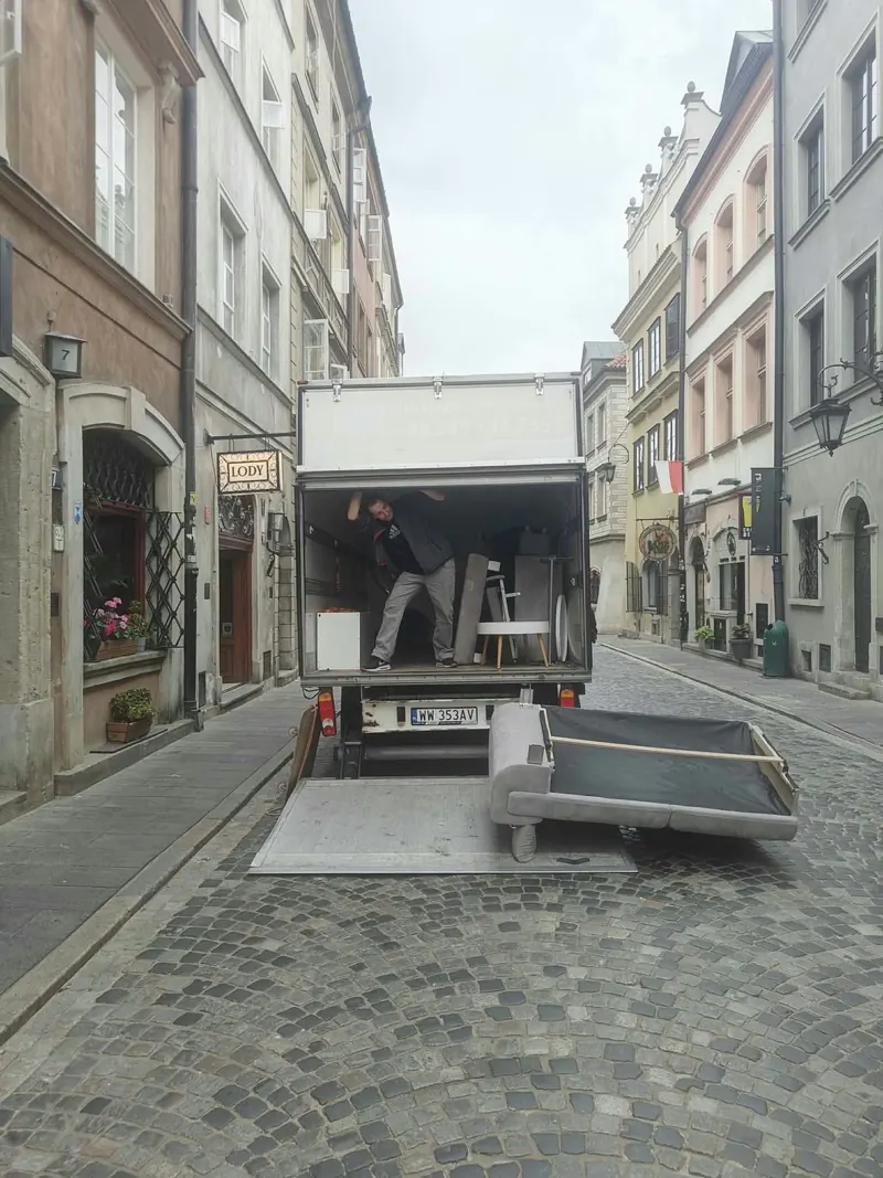 Auto BP Meble z opuszczoną windą załadowczą podczas odbioru kanapy na brukowanej uliczce w centrum Warszawy